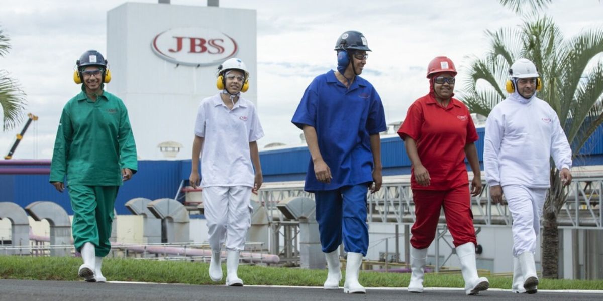5 funcionários com seus uniformes em frente à fábrica da JBS