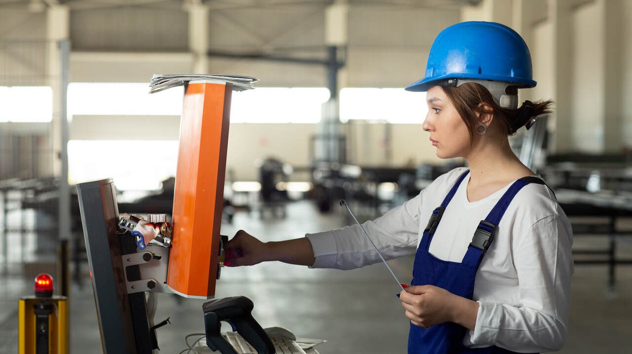 Mulher de capacete operando máquina em fábrica enquanto trabalha de Jovem Aprendiz