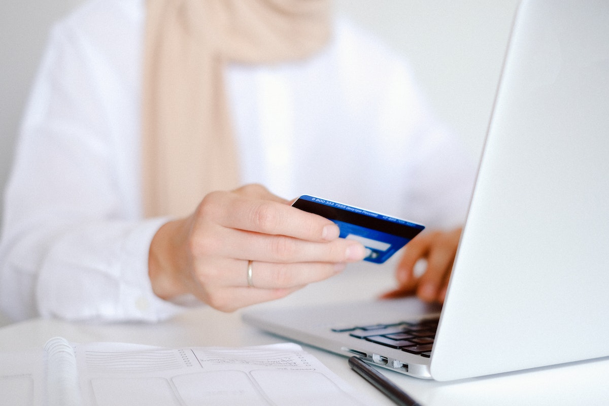Pessoa com cartão de crédito na mão, realizando compra no computador